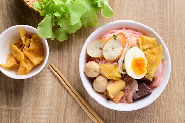Thai food (Yen Ta Fo), Rice noodles soup with red sauce and fish tofu, pork ball and fried wonton in a bowl with chopsticks on wooden background, Top view