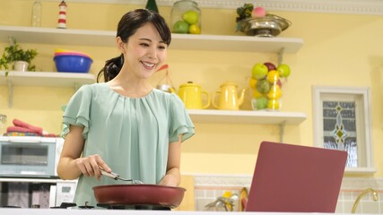 パソコンを見ながら料理をする女性