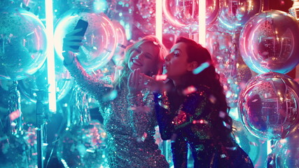 Blonde and brunette women sending kisses in club. Girls making selfie at party