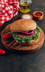 Homemade burger with black angus beef meat and fresh vegetables on a wooden board.