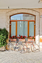 Fototapeta na wymiar Italian building on a cobblestone street with bicycles and flowers in front of a big window. No people