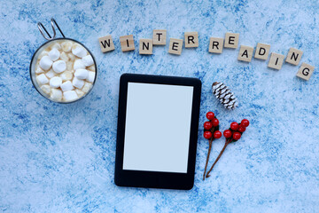 Winter and Christmas themed top view of an ebook, marshmallow hot chocolate, and Christmas...