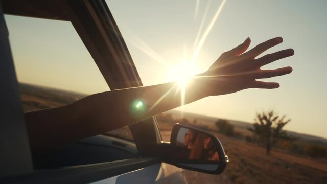 free girl hand out of the window rides a car wind in the face. concept car travel on the road. girl stretches her hand out of the car window sun glare sunset. driver hand out of the window movement