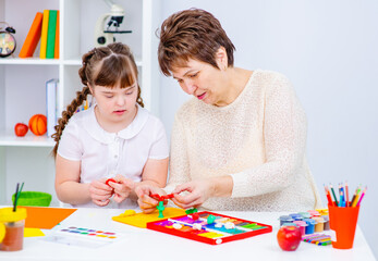 The teacher shows the student with down syndrome how to do creativity. Girl with down syndrome smiles at teacher