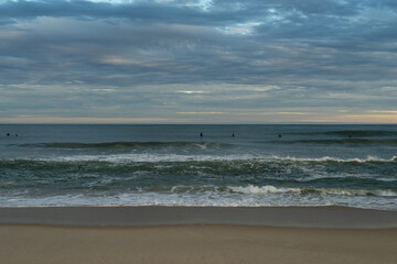 Surfers bob in the ocean at sunset