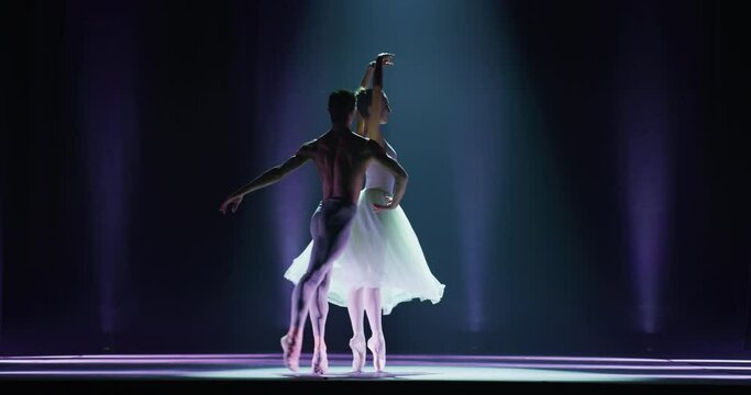 Cinematic shot of young couple of classical ballet dancers is performing a choreography on classic theatre stage with spotlights before start of a show.