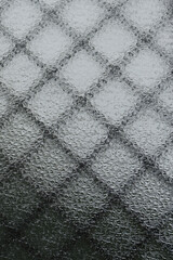 Translucent window of opaque textured glass with diamond grid behind the glass