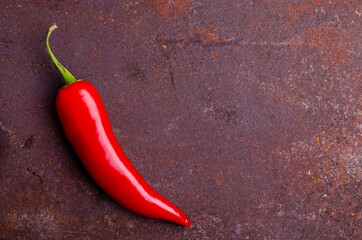Red pepper pod on a rusty brown metal background.