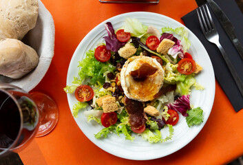 Appetizing salad with goat cheese and prosciutto served on plate