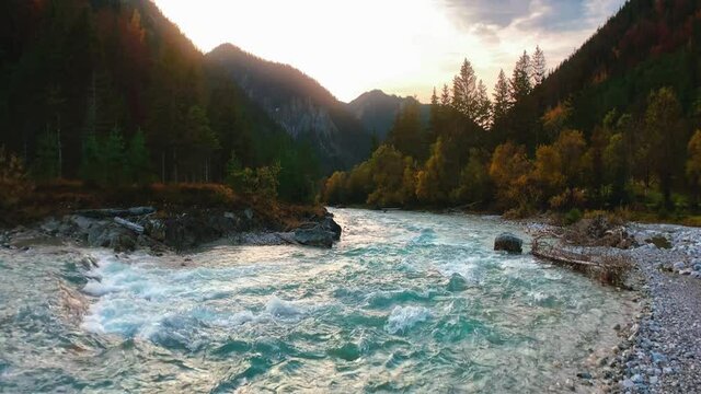 4K UHD seamless anamorphic cinema ratio video of a mountain river in the Austrian alps with a vibrant evening sky, close to the German border in autumn. The water is rushing along colorful fall trees.