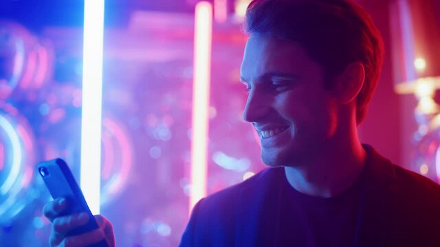 Handsome man using smartphone in nightclub. Smiling guy dancing at party