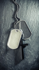 US military soldier's dog tags, rough and worn with blank space for text, and Christian cross necklace. Memorial Day or Veterans Day concept.