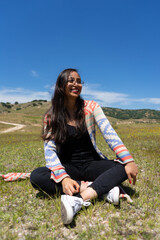 woman with glasses, long hair, black blouse and sweater smiling in a park