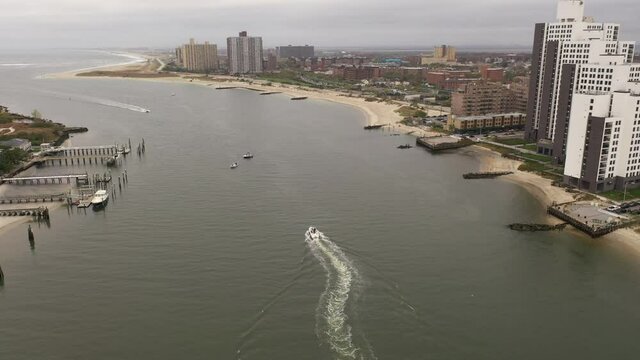 A high angle view over East Rockaway Inlet as a boat head out to sea leaving a white wake behind. The camera dolly in following the boat on a cloudy morning that is peaceful & the water is calm.