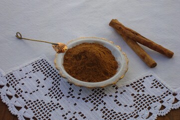 Canela en polvo en plato de cerámica, cucharilla de latón y dos trozos de canela entera sobre...