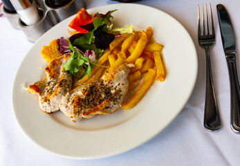 Spiced herb baked chicken fillet with side dish of crispy fries and vegetables