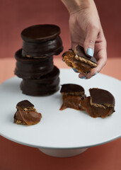 Torre de alfajores rellenos de dulce de leche bañados en chocolate mano sosteniendo un trocito de alfajor