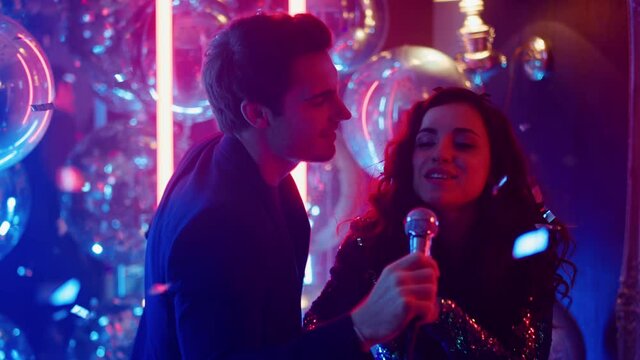 Smiling couple performing song at party. Man holding microphone in nightclub
