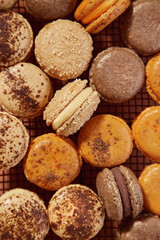 vista cenital de macarons franceses beige, naranja y marron sobre rejilla negra de alambre en fondo de terracota