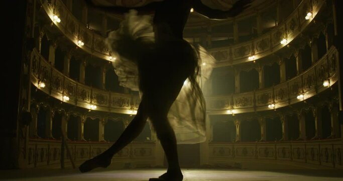 Cinematic close up shot of an young graceful classical ballet female dancer in white tutu is performing a choreography on classic theatre stage with dramatic lighting before start of a show.