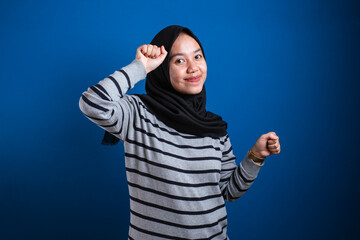 Portrait of a funny young Asian muslim girl wearing hijab dancing happily joyful expressing celebrating good news