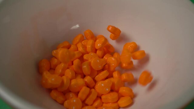Extreme close up of orange skull shaped candy falling on a white plate.