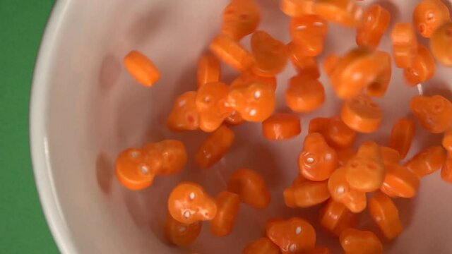Close up of orange skulls and bones shaped candy falling on a plate, on a chroma background.