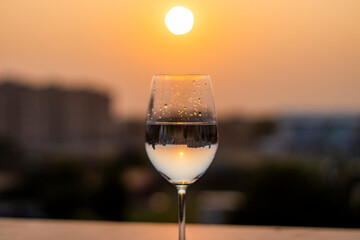 Clear liquid being poured into a wine glass at sunset