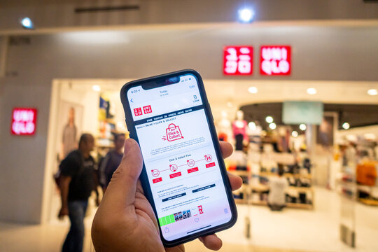A man's hand holding an iphone X with uniqlo apps infront of Uniqlo store.