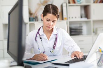 Focused woman doctor working with laptop in clinic office. Modern medicine and healthcare concept