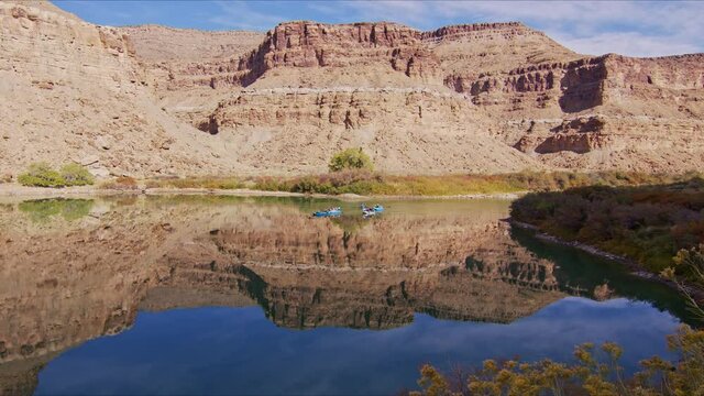 Group of people rafting the Green River through the glassy reflection of the Book Cliffs in the Utah desert during Fall.