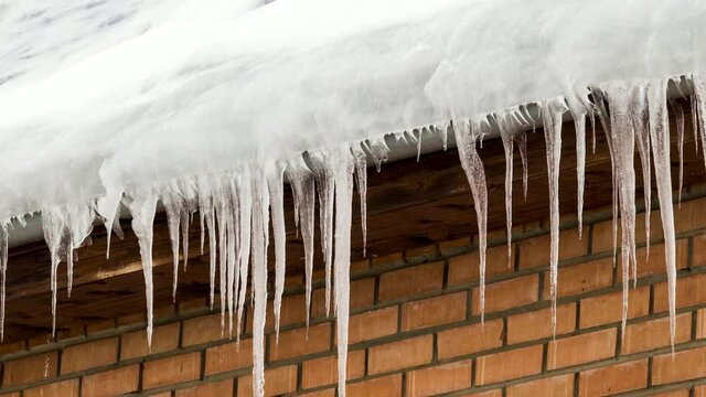 Lots of large icicles on the roof of a brick house.