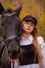  portrait of a girl with blonde hair and a Bay horse on the background of an autumn forest.