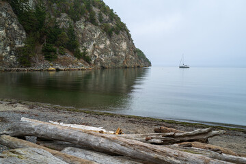 Fototapeta na wymiar Sailboat anchored off the driftwood lined shore of Watmough Bay on Lopez Island, Washington, USA