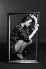 A young woman poses inside a picture frame. Black and white Studio photo.