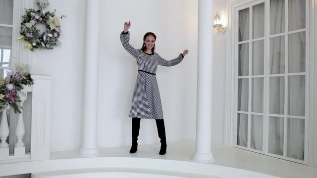 elegant young girl in a dress posing next to a column and a large window of the house, slow motion