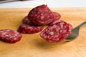 Slices of delicious smoked sausage on a wooden background. Prick one slice on a fork