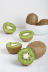 Halved ripe green kiwi fruit slices full of vitamin C and antioxidant served on white wooden background with bowl at kitchen representing healthy dieting and lifestyle. Vertical orientation image