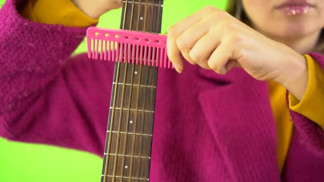 Female Hands With A Pink Comb Combing A Guitar, Surrealism On A Green Background, Close-up. Advertising Concept, Guitar Tuning, Psycho.