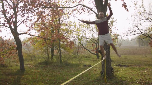 Caucasian man practicing slackline in the autumn forest. A man practices highlining in the autumn forest at dawn.