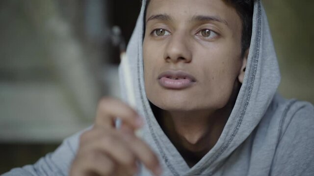 Close-up face of mixed-race boy with brown eyes blowing out match and looking at camera. Portrait of thoughtful depressed teenager planning setting fire. Adolescence and crime concept.