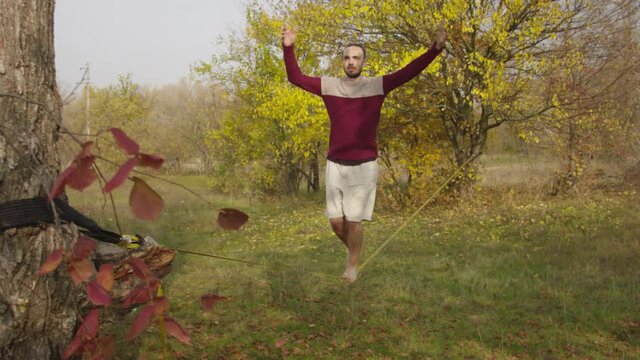 Caucasian man practicing slackline in the autumn forest. A man practices highlining in the autumn forest at dawn.