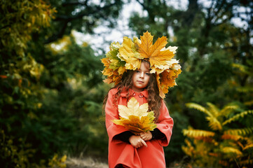 Portrait of a romantic little girl in an autumn Park . A child in a coat and a wreath of maple...