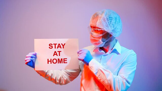 A male doctor is holding a poster with the inscription: Stay home.