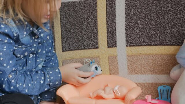 a little and cute girl plays with a doll and a hedgehog on the sofa. The toys are wearing protective masks. The bobblehead sleeps on the couch, and the hedgehog sings a lullaby.