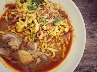 Khao Soi Kai, Thai spicy food in white blow on wooden table, Thai spicy soup. Thai Food. Northern Thai Style Curried Noodle Soup with Chicken