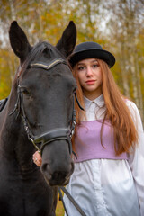 Obraz premium Red-haired girl in a black hat with a horse in the autumn forest.