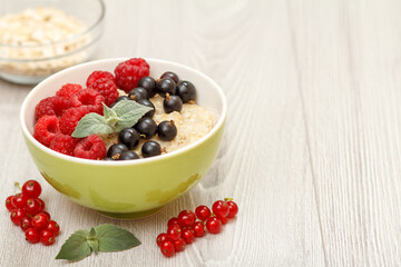Oatmeal porridge in porcelain bowl with currant berries