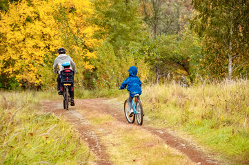Family cycling in golden autumn park, active father and kids ride bikes, family sport and fitness outdoors
