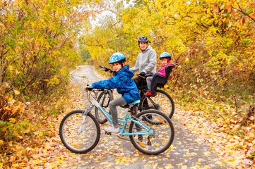 Family cycling in golden autumn park, active father and kids ride bikes, family sport and fitness outdoors
